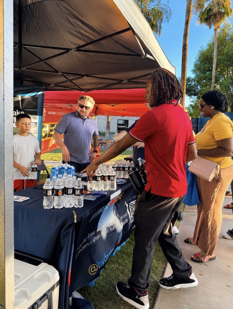 Community members approach the Hydrate PHX booth as a volunteer hands out water.