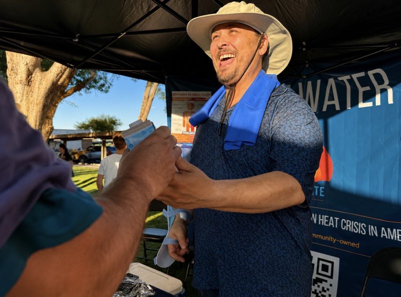 A Hydrate PHX volunteer smiles while handing out cooling supplies at a distribution event.