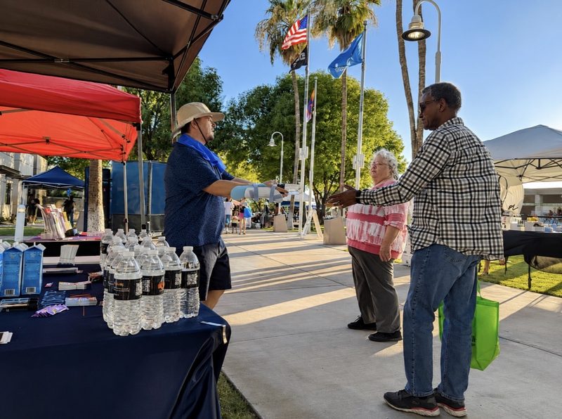A Hydrate PHX volunteer hands water to an older couple at the distribution booth.