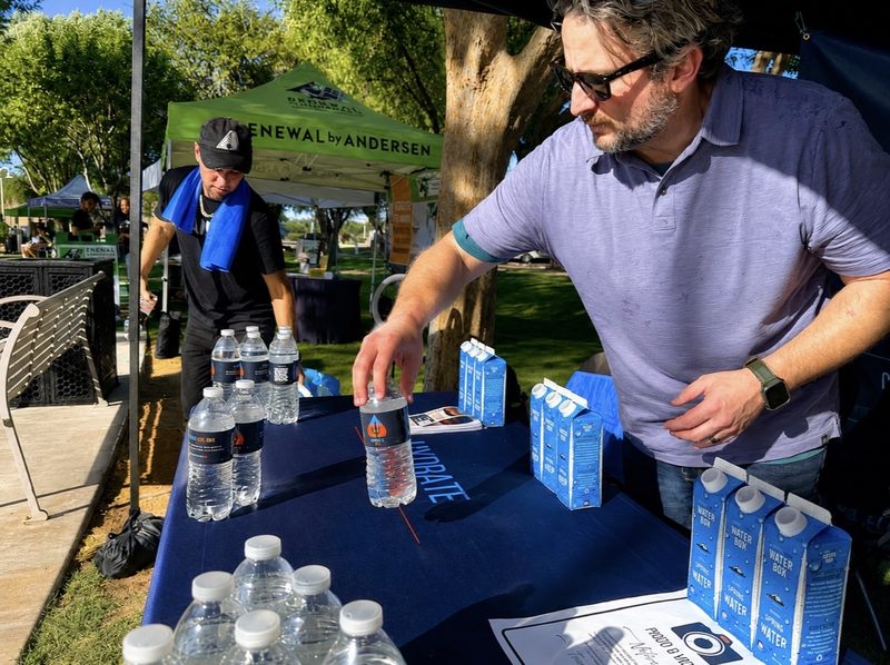 Two volunteers arrange water bottles and cartons on the distribution table before doors open.